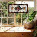 30"L Fleur De Lis Stained Glass Pub Window Panel hanging in window above a wooden window sill with plants.