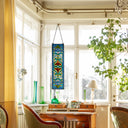 36"H Victorian Stained Glass Fleur De Lis Window Panel hanging above a wooden desk in a sunlit room with large windows.