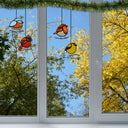 4.5" H Bird Quartet Stained Glass Window Panel Set hanging in front of a window with trees outside.