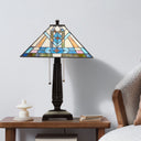 21" H Amberly Tiffany-Style Stained Glass Empire Shade Candlestick Table Lamp, styled on a wooden side table next to a white candle and books, with a textured armchair visible on the right.