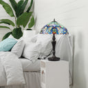 24.5" H Marlowe Multicolor Tiffany-Style Stained Glass Table Lamp, styled on a white bedside table next to a bed with white linens and a green houseplant.