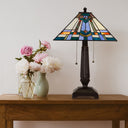 21" H Clarion Tiffany-Style Stained Glass Empire Shade Candlestick Base Table Lamp, styled on a wooden table next to two vases of pink and white flowers against a plain white wall.