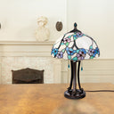 Tula 24.75" H Tiffany-style Teal Bowl Shade Stained Glass Table Lamp on a wooden surface, with a fireplace and statue in the background.