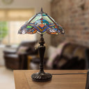 24" H Highclere Victorian Multicolor Tiffany-Style Stained Glass Table Lamp, shown sitting on a wooden table in a softly blurred living room setting.